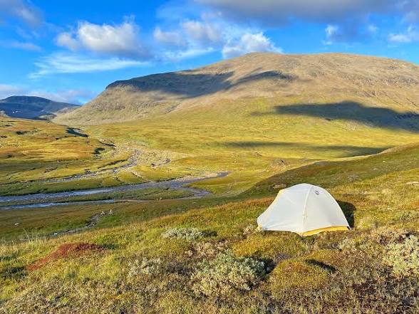 Tent pitched on golden autumn tundra with a wide mountain backdrop.