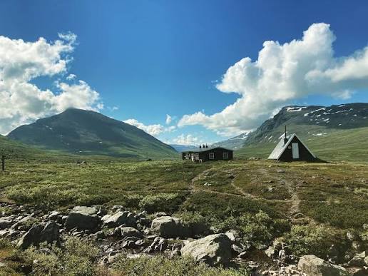 STF hut and a tent pitched in a green valley beneath fjäll peaks.
